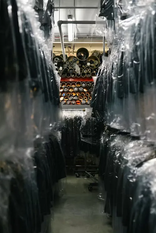 Finished garments in protective covers beside fabric rolls in our storage area